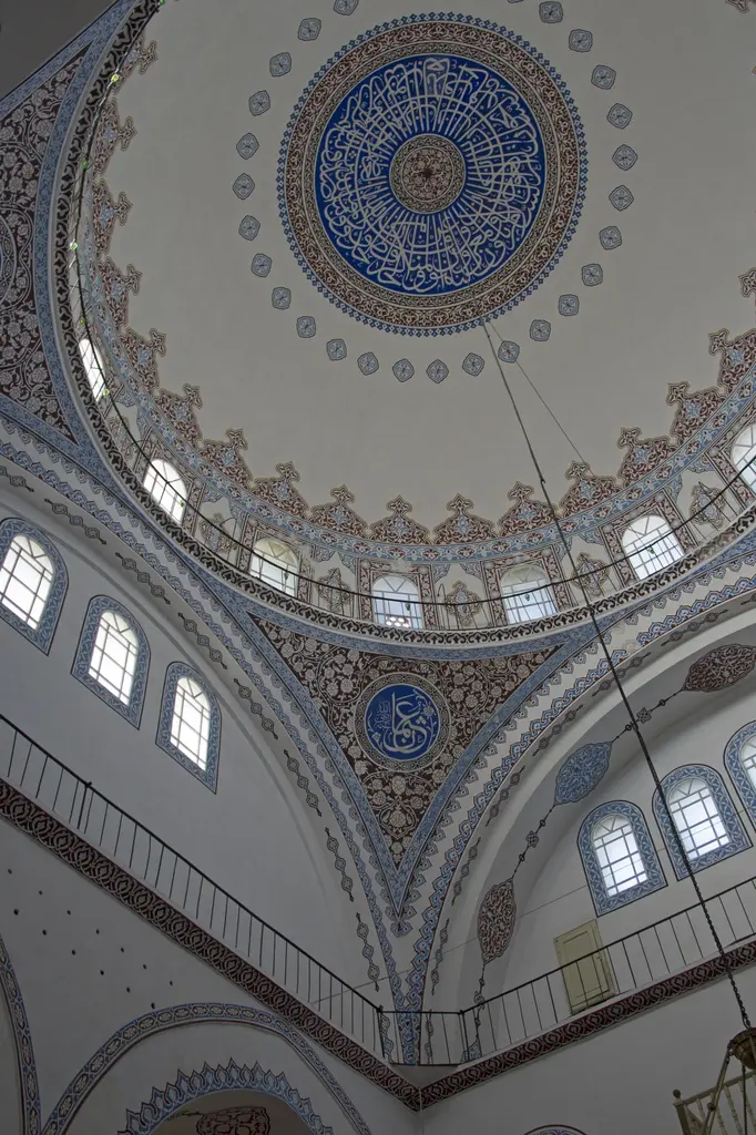 Gazi Atik Ali Paşa Camii'nin kubbesi içten; ortada mavi yazılı göbek, çevresinde kalem işi kuşak, kasnak pencereleri ve kemerler.