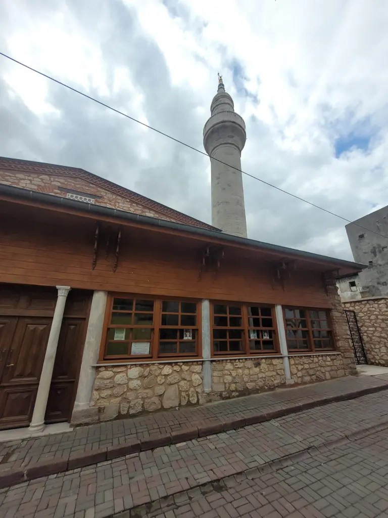 Atik Mustafa Paşa Camii'nin ahşap son cemaat yeri; geniş ahşap saçak, sıra hâlinde ahşap doğramalı pencereler, moloz taş kaide, arkada tuğla gövde ile taş minare.