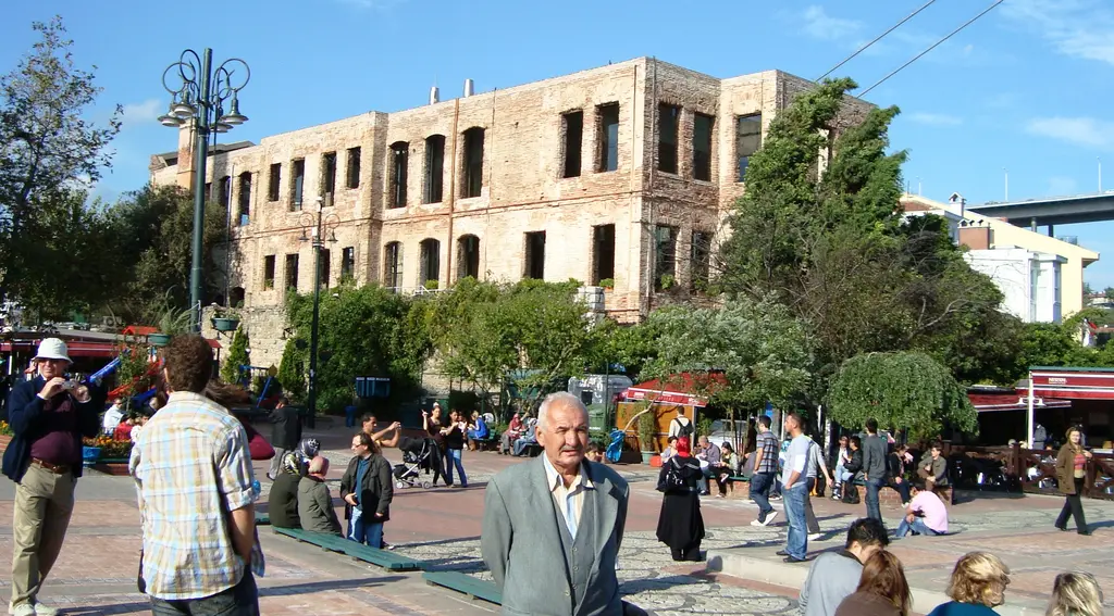 Ortaköy meydanından Esma Sultan Yalısı; meydanda yürüyen insanlar, ağaçlar, fener direkleri ve arkada köprü.