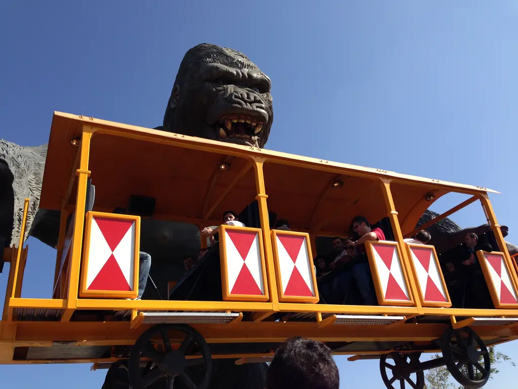 Vialand'de King Kong ünitesi; dev goril figürünün altında sarı ve kırmızı vagonlu tren, içinde oturan ziyaretçiler ve mavi gökyüzü.