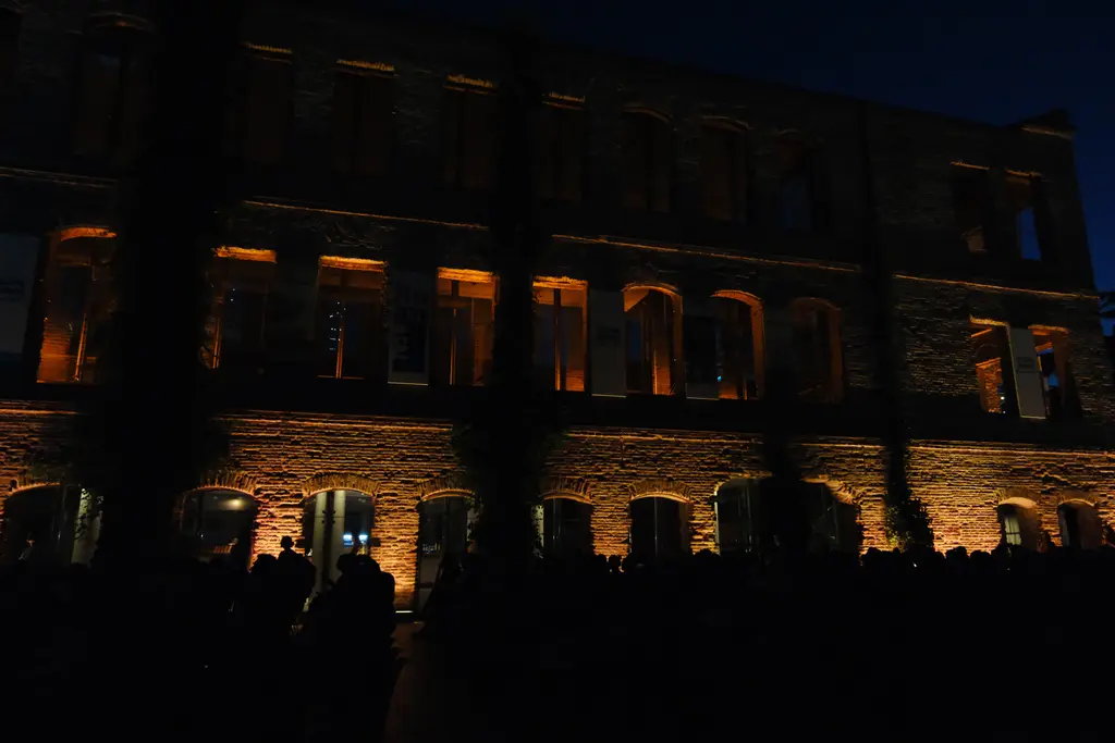 Esma Sultan Yalısı'nın uzun cephesi gece; sıra sıra ışıklı pencere boşlukları, taş duvarlar ve önde karanlık siluetler.