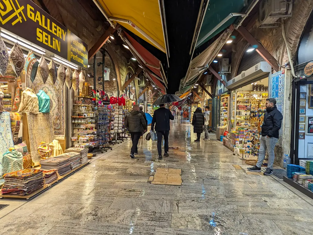 Arasta Çarşısı'nın dükkânlarla çevrili sokağı; tentelerin altında halı ve hediyelik eşya vitrinleri, parlak taş zemin ve yürüyen insanlar.