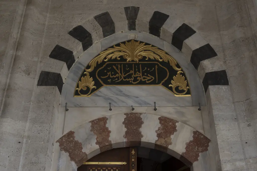 Mihrimah Sultan Camii'nde yan kapı; kesme taş duvar, kemerli kapı açıklığı ve üstünde yazılı bir pano.