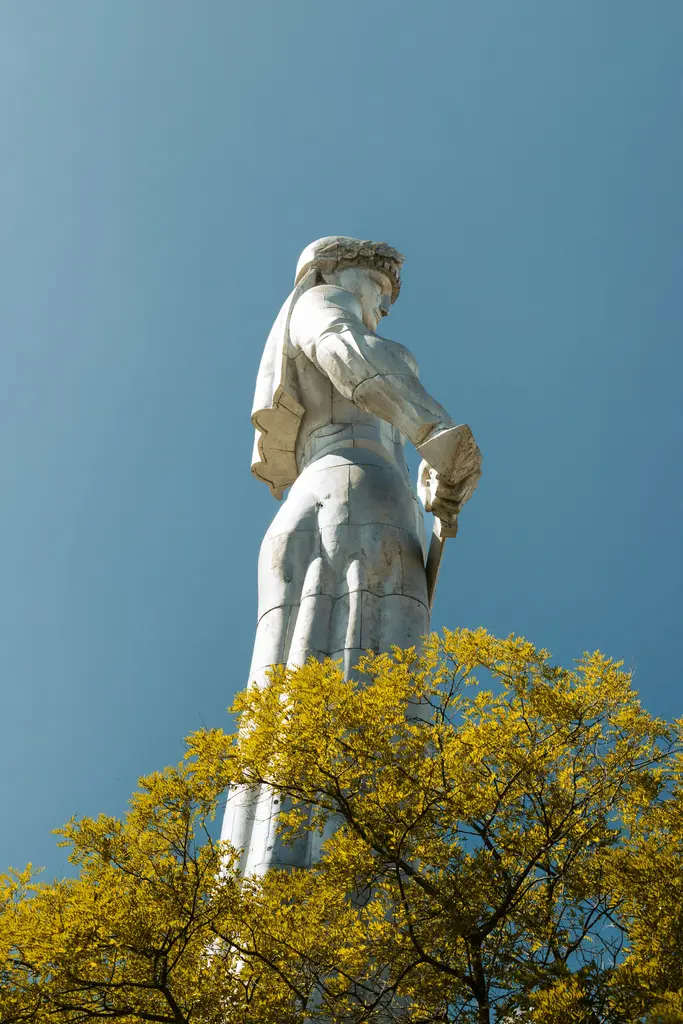 Tiflis'te bir elinde kâse diğerinde kılıç tutan Gürcistan Anası (Kartlis Deda) alüminyum heykeli; ardında açık gökyüzü.