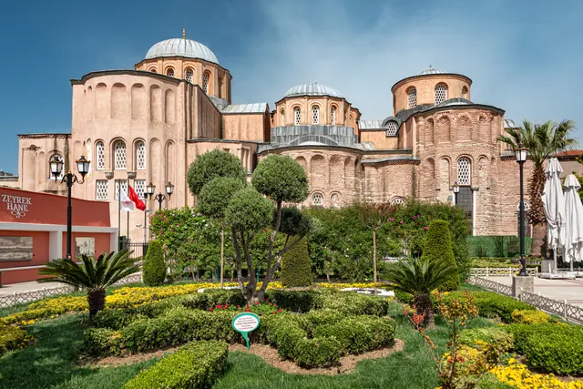 Fatih'te Zeyrek Camii bahçeden; yan yana dizilen yuvarlak apsisler, kurşun kaplı küçük kubbeler, tuğla ile taşın dönüşümlü örüldüğü pembemsi cephe ve önde budanmış yeşil bahçe.