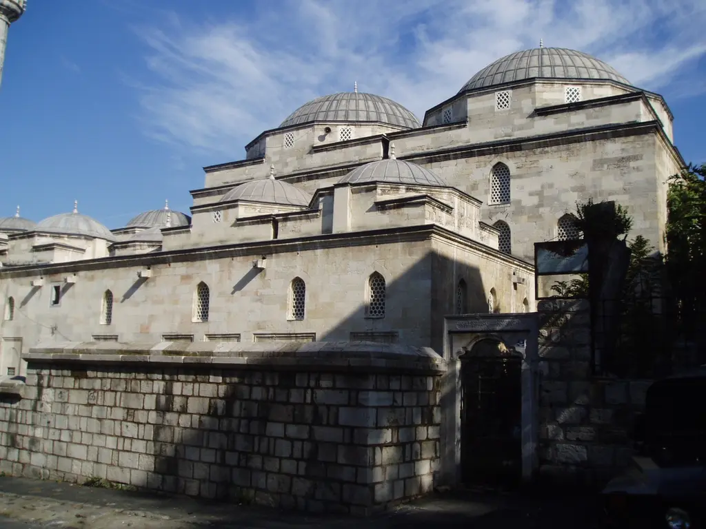 Mahmut Paşa Camii'nin kubbeleri; yüksek taş avlu duvarının ardında kademe kademe yükselen kurşun kubbeler, taş gövde ve mavi gökyüzü.