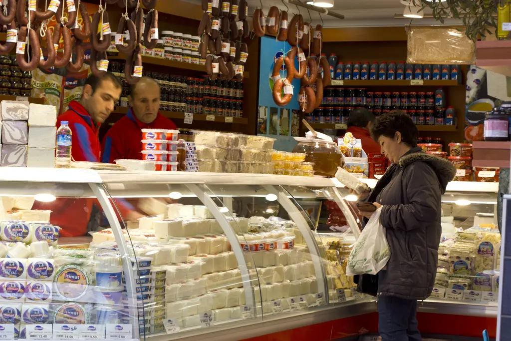 Kadıköy Çarşısı'nda şarküteri; vitrinde beyaz peynirler, tavanda asılı sucuklar, satıcılar ve müşteri.