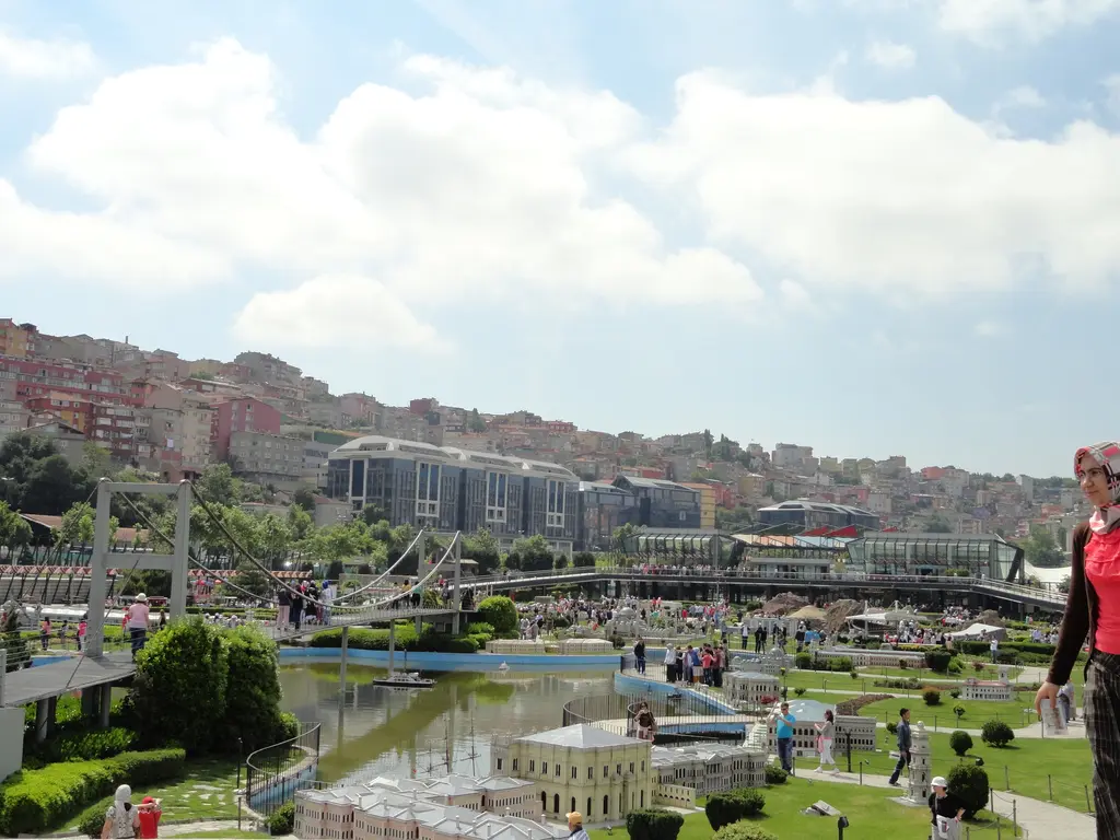 Miniatürk'te maket havuzu; suyun üstünde asma köprü maketi, kıyıda açık sarı saray ve yalı maketleri, yollarda ziyaretçiler.