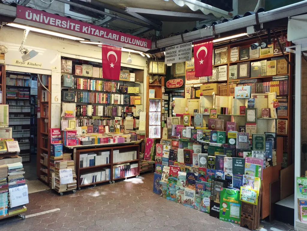Sahaflar Çarşısı'nda bir kitabevinin iç mekânı; üstte "üniversite kitapları bulunur" bandı, içeride sarkan iki Türk bayrağı, ahşap tezgâh ve arkasında zeminden tavana kitap rafları.