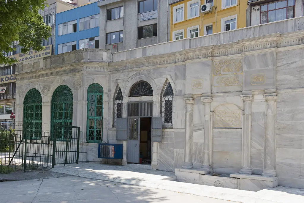 Oğlanlar Tekkesi sebili; mermer cephede yuvarlak kemerli yeşil demir şebekeli pencereler, ortada kapı ve yanında avlu.
