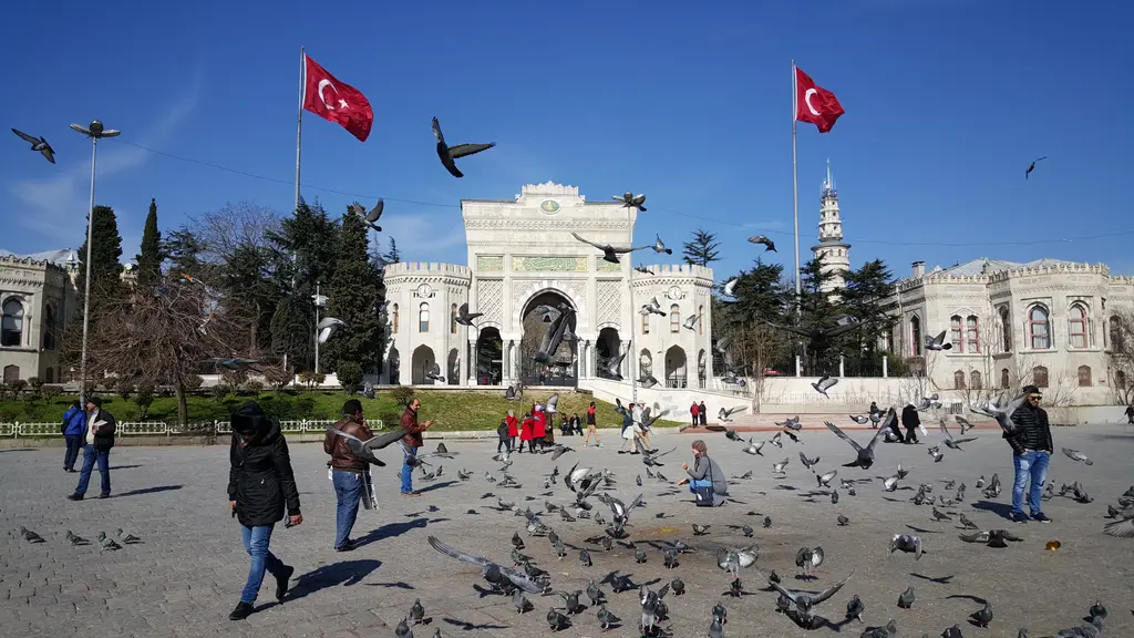 Meydandan Beyazıt Kulesi; önde güvercin sürüsü ve yürüyen insanlar, ortada üniversite kapısı, arkasında ağaçlar ile kule.
