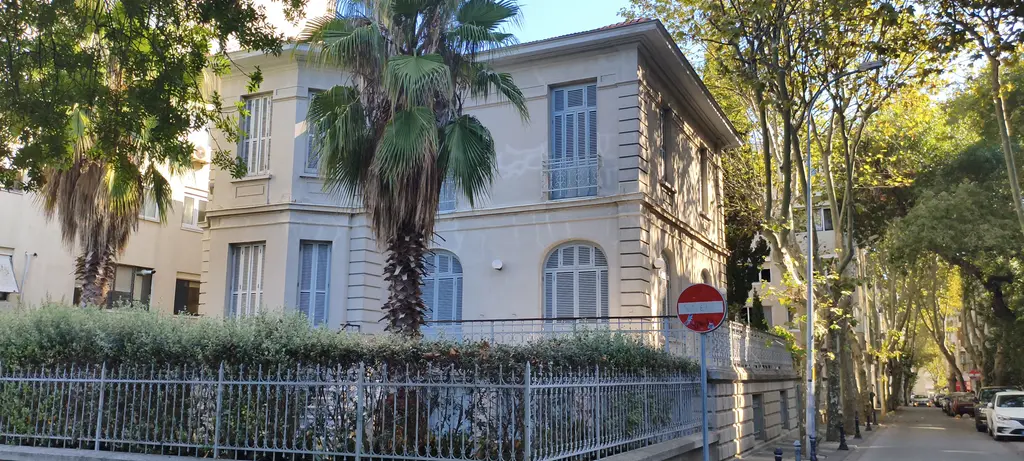 Moda'da Antipa Köşkü; krem rengi iki katlı köşk, palmiye ağacı, bahçe çiti ve ağaçlı sokak.