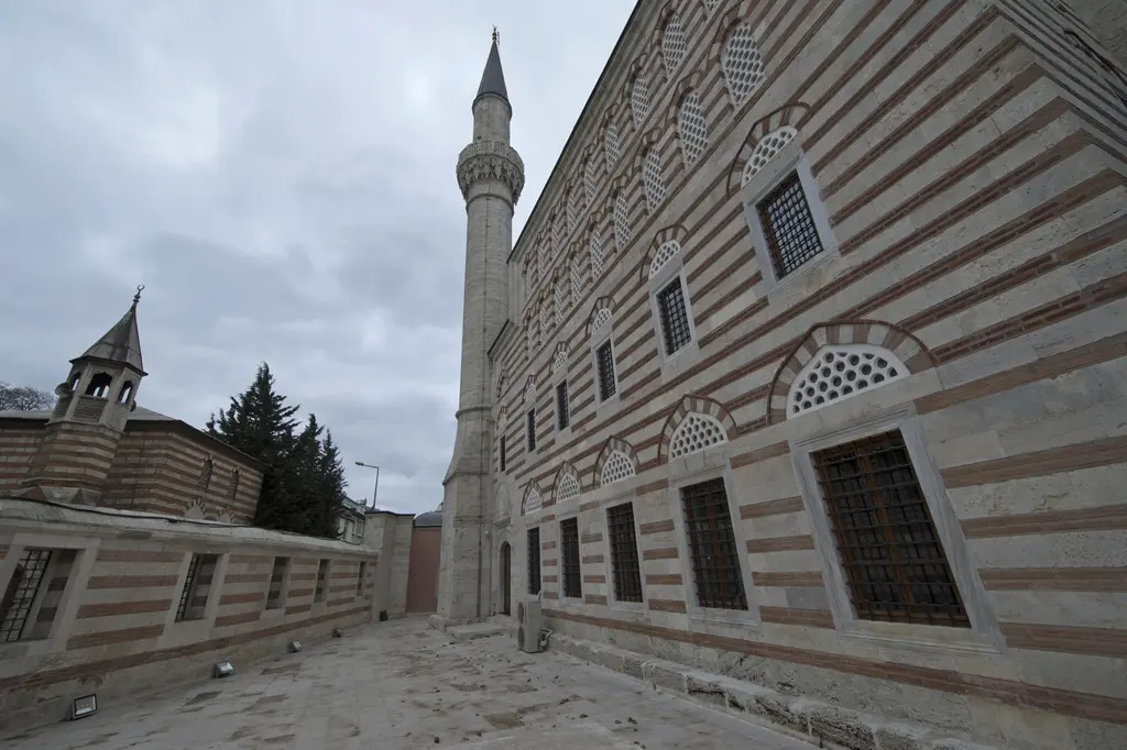 Zal Mahmud Paşa Camii'nin dış duvarı; geniş açıyla taş ve tuğla sıralı cephe, demir parmaklıklı pencereler, minare ve bulutlu gökyüzü.