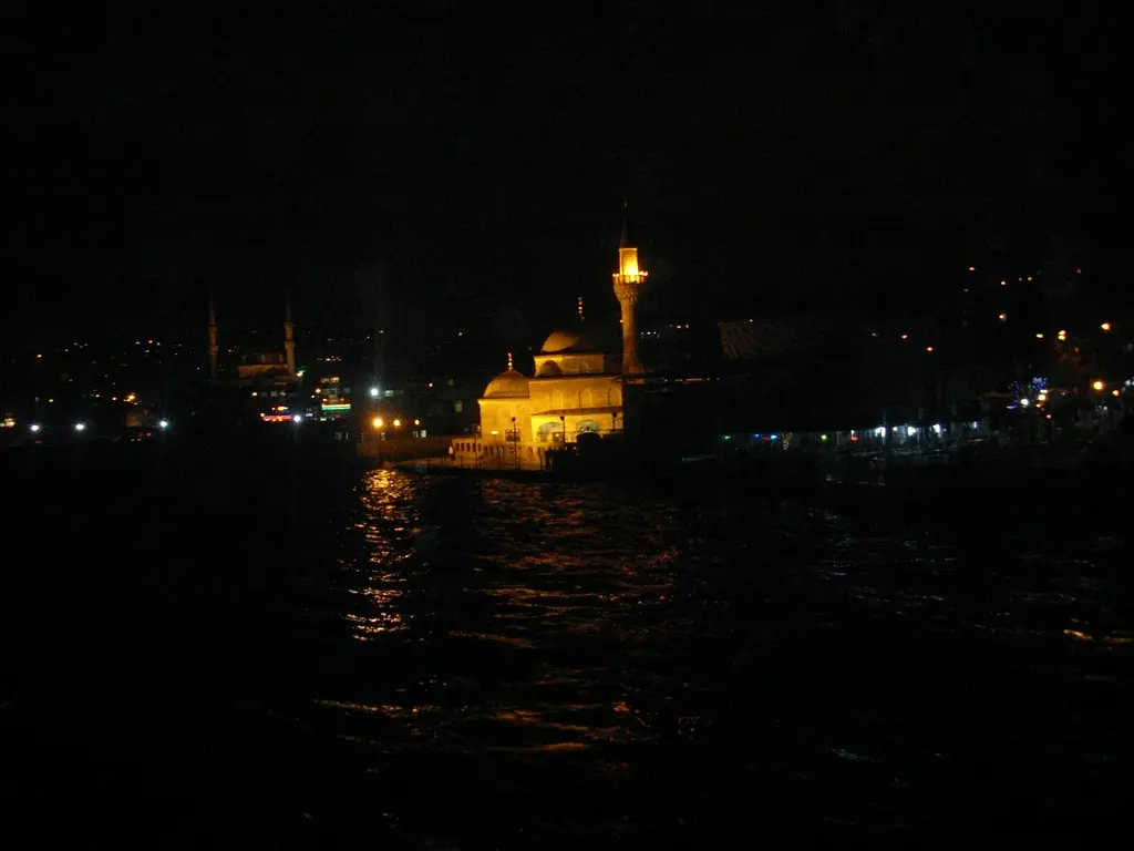 Gece Şemsi Paşa Camii; karanlık denizin kıyısında sarı ışıkla aydınlatılmış kubbe ve minare.