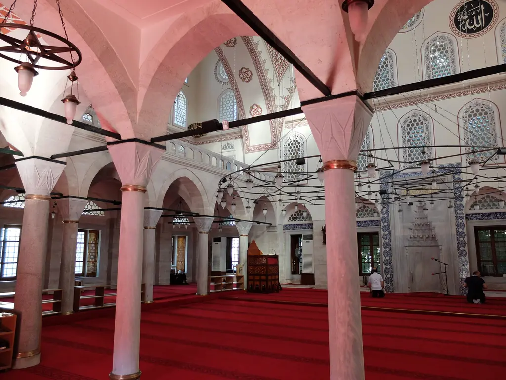 Zal Mahmud Paşa Camii'nde mahfil sütunları; ince mermer sütunlar, pembe ışıkla aydınlanan tonozlar, kırmızı halı ve namaz kılanlar.