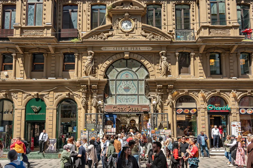 İstiklal Caddesi'nde Çiçek Pasajı'nın cephesi; heykelli ve süslü taş ön yüz, ortadaki kemerli giriş ve önünde toplanan kalabalık.