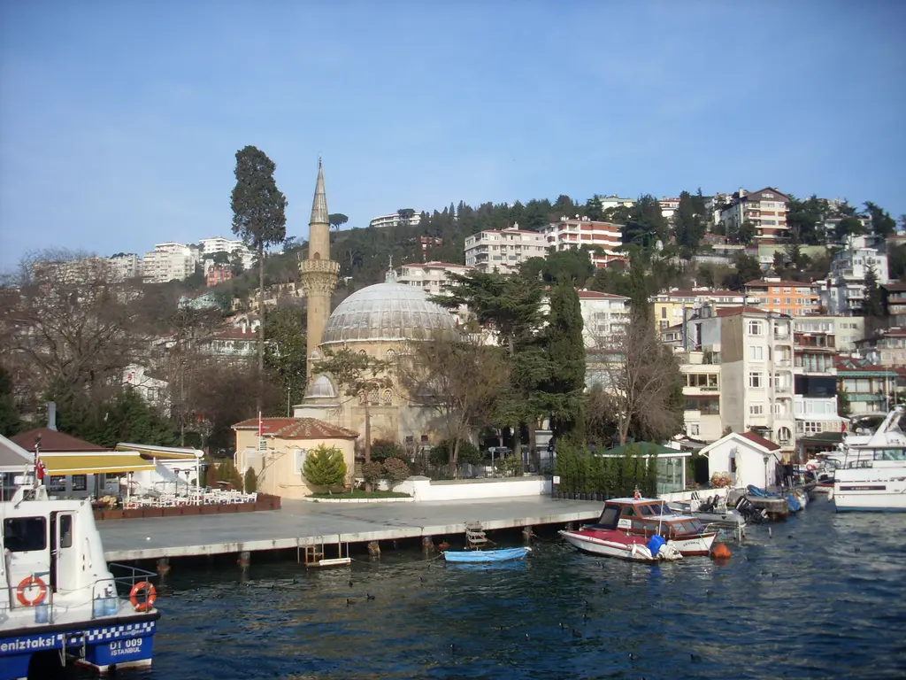 Bebek'te denizden cami ve iskele; kurşun kaplı kubbe, ince minare, önde rıhtıma bağlı tekneler ve iskele.