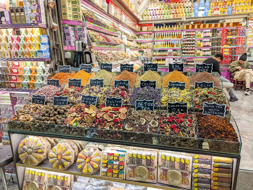 Sultanahmet'te bir çarşı tezgâhı; bölmelerde yığılmış renkli baharatlar ile kuru meyveler, önde tepsilerde lokum ve arkada dolu raflar.