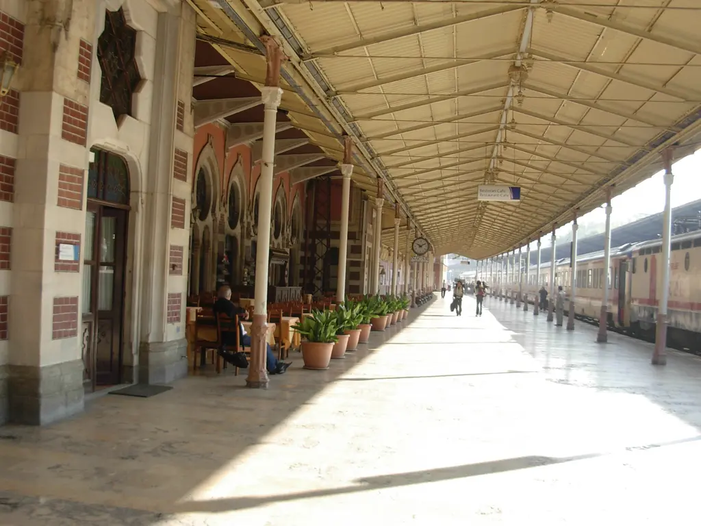 Sirkeci Garı'nda güneşli peron koridoru; solda sekiz kollu yıldız kabartmalı taş duvar, kemerli kapı ve saksılar, sağda beyaz demir sütun dizisi, ileride bekleyen bir tren.