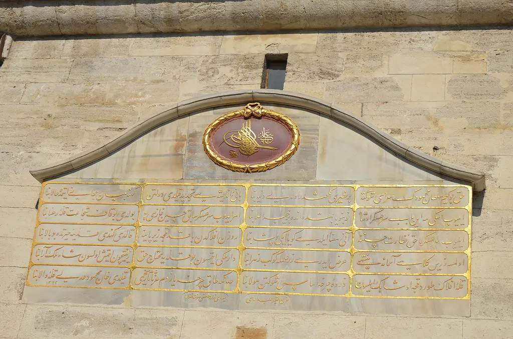 Beyazıt Kulesi'nin kitabesi; mermer pano üzerinde altın yaldızlı satırlar, üstünde madalyon içinde padişah tuğrası ve profilli çerçeve.