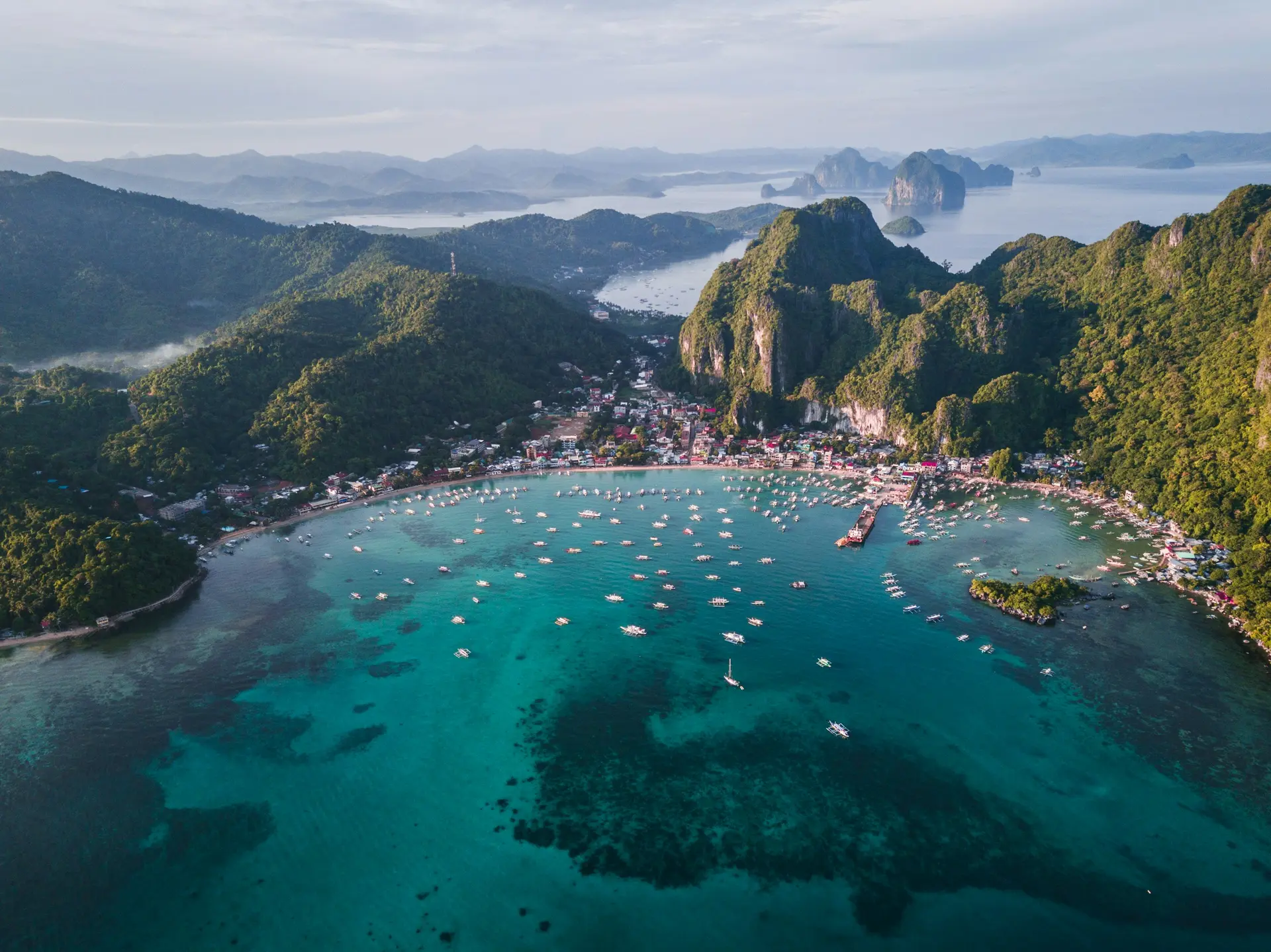 Tayland'da Phi Phi Adaları; yeşil tepelerle çevrili turkuaz koy, kıyıdaki yerleşim ve suda demirli yüzlerce tekne.