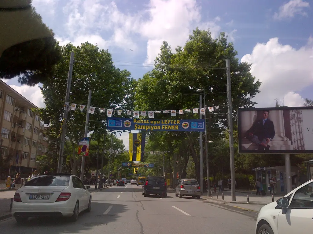 Bağdat Caddesi üzerinde Fenerbahçe flamaları; çınar ağaçları, yolda arabalar ve ağaçlar arasına asılmış sarı lacivert pankart.