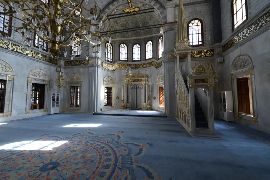 Nusretiye Camii'nin içi; desenli mavi halı, ortada mihrap, sağda minber, yukarıda büyük avize ve kemerli pencere sıraları.