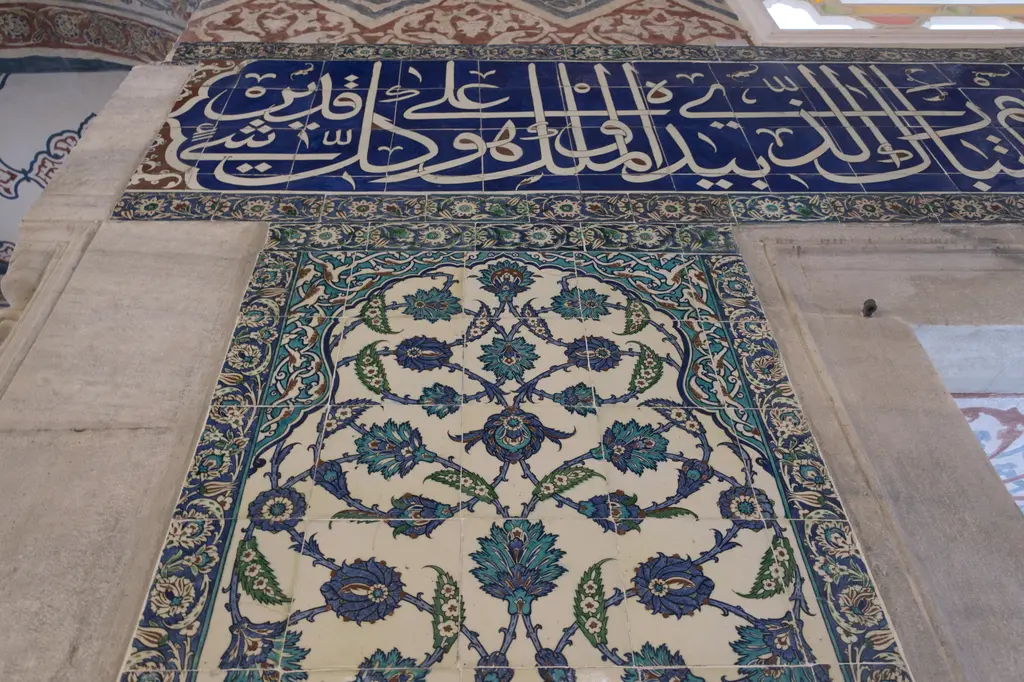 Sultan Ahmed Türbesi'nde çini kitabe kuşağı; lacivert zemin üzerine beyaz yazı, altında bitkisel desenli çini pano ve mermer pencere sövesi.