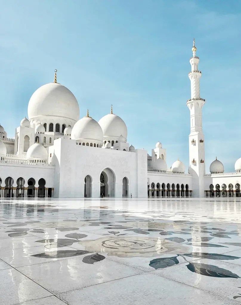 Abu Dabi'de Şeyh Zayed Camii; bembeyaz mermer kubbeler, minareler ve yansıma havuzu, akşam ışığında.