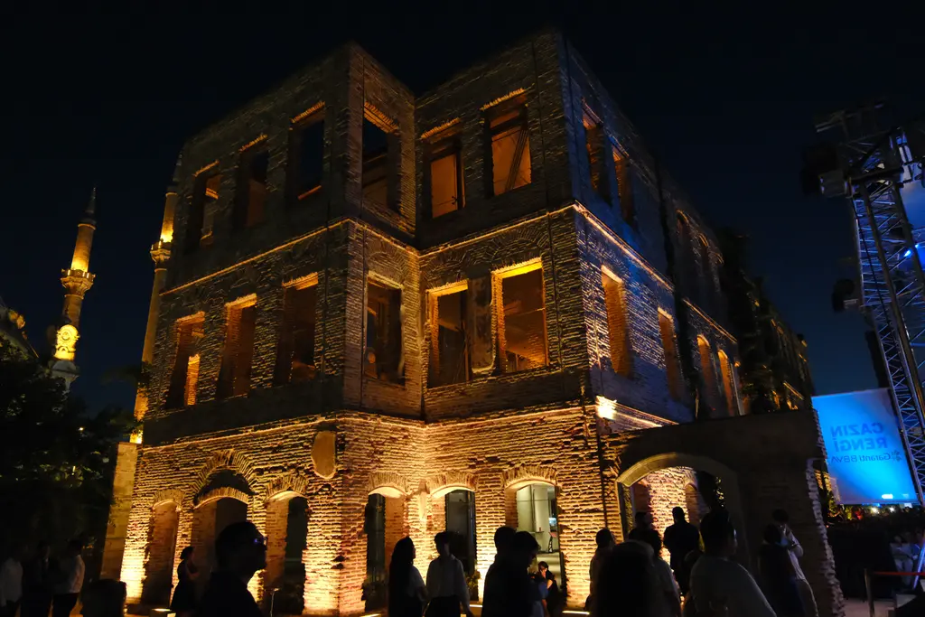 Gece Esma Sultan Yalısı; turuncu ışıkla aydınlatılmış taş cephe, arkada aydınlık minare ve önde kalabalık.