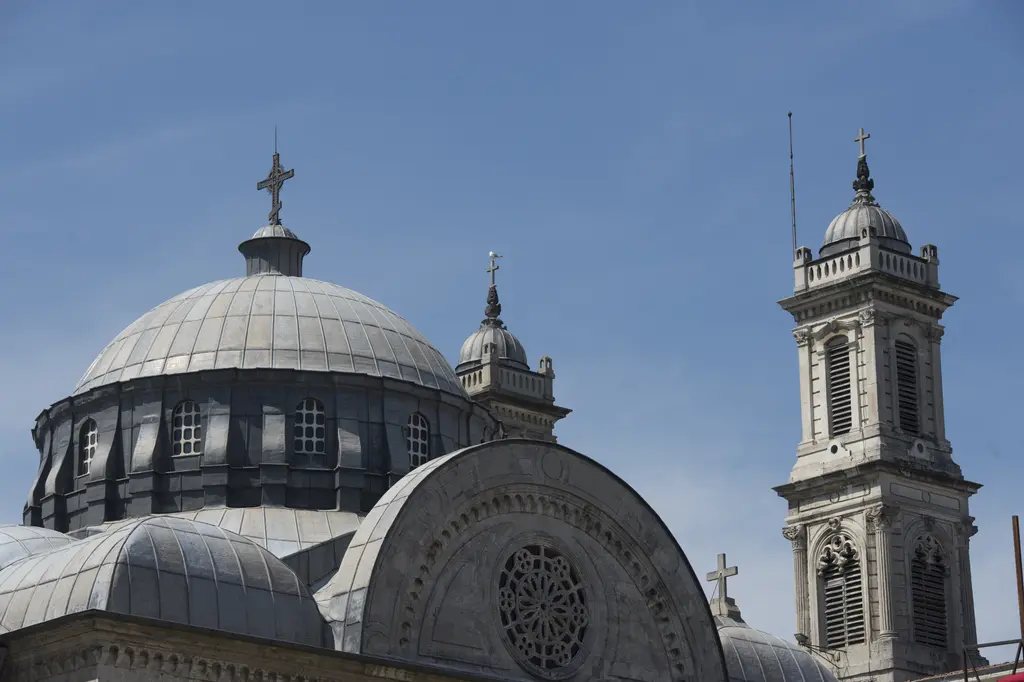 Aya Triada Kilisesi'nin kubbesi ve çan kulesi; kurşun renkli kubbe, tepede haç, yanda kubbeli kule ve mavi gökyüzü.