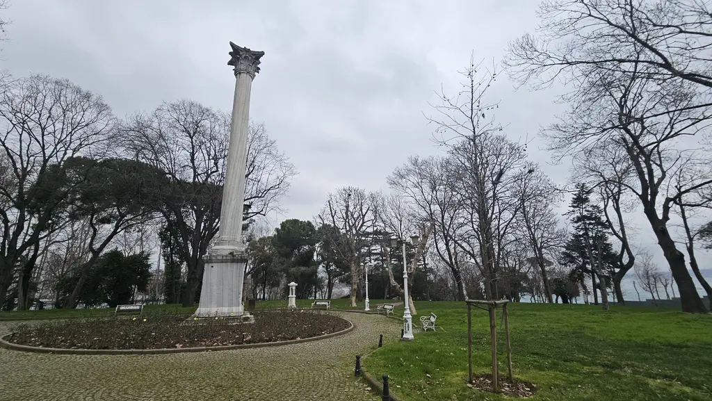 Kışın Gülhane Parkı'nda Gotlar Sütunu; önde halka biçimli toprak tarh, parke yol, çimenlik, yapraksız ağaçlar ve bulutlu gök.