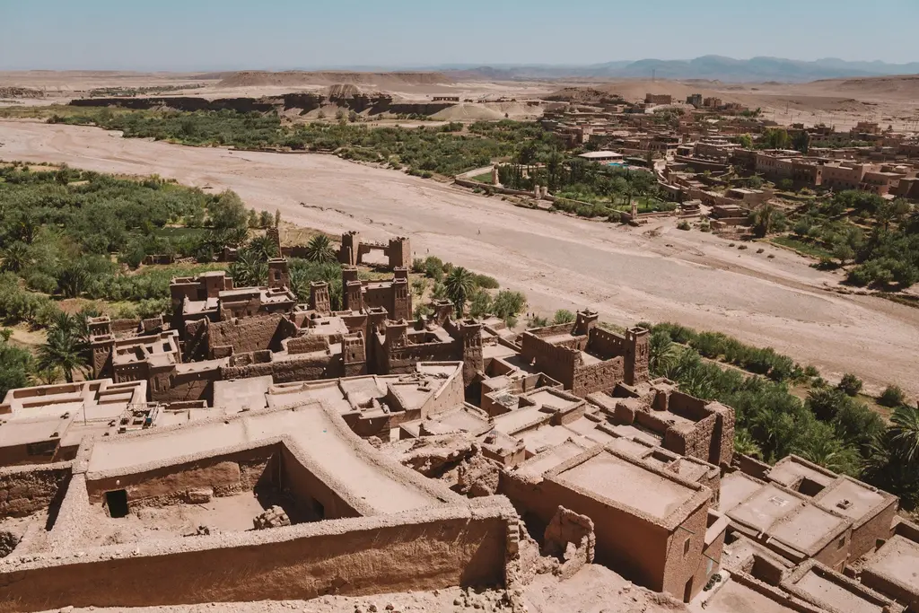 Fas'ta Ait Benhaddou'nun toprak kalesi; yukarıdan bakışla kerpiç yapılar, kuru nehir yatağı ve arkada palmiyelik ile çöl.