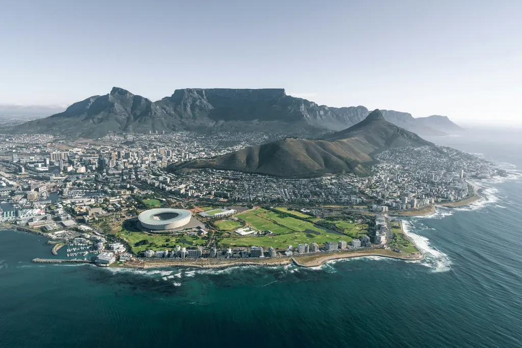 Güney Afrika'da Cape Town'ın kuş bakışı görünümü; arkada düz zirveli Masa Dağı, önünde şehir ve yeşil alanlar, iki yanda kenti saran Atlas Okyanusu.