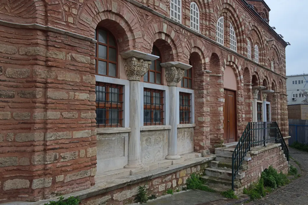 Vefa Kilise Camii'nin revakına kuzey ucundan çapraz bakış; üç kemerli göz, sepet biçimli oyma başlıklar, parmaklıklı kırmızı doğramalar ve rozetli mermer levhalar.