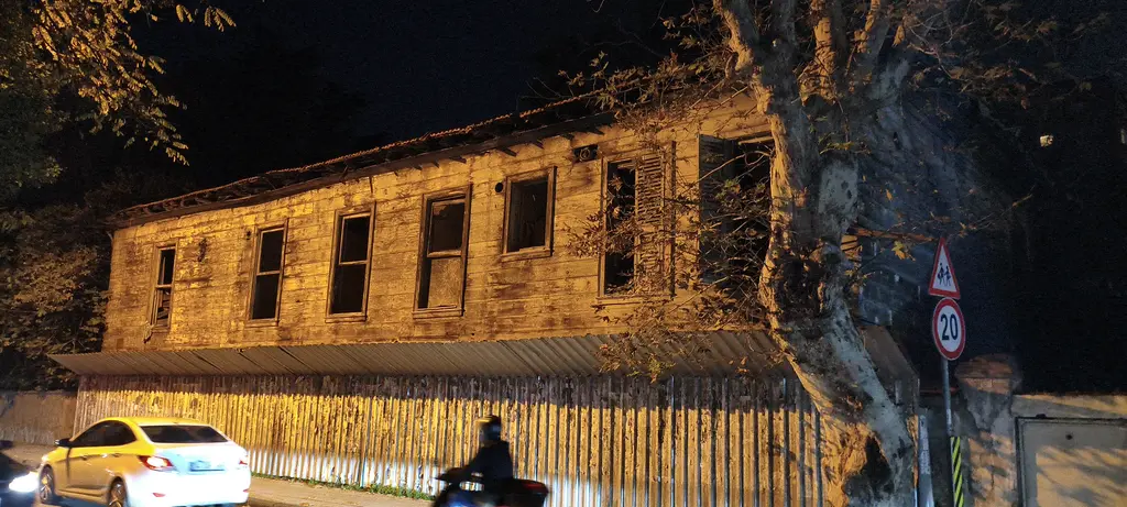 Göztepe'de gece Rıdvan Paşa Köşkü'nün ahırları; sokak ışığıyla aydınlanan ahşap yapı, önünden geçen taksi ve motor.