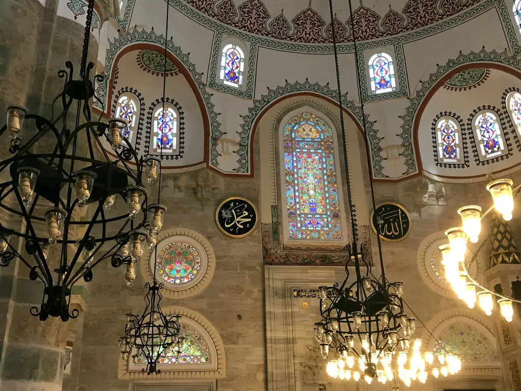 Mihrimah Sultan Camii'nde avizeler; demir avize halkaları, renkli camlı pencereler ve kalem işli kemerler.