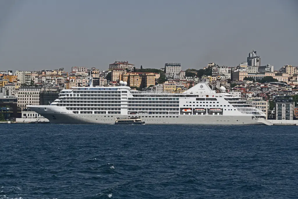 Galataport'ta yanaşmış beyaz kruvaziyer gemisi; arkada Tophane yamacındaki binalar, önde mavi Boğaz suyu.