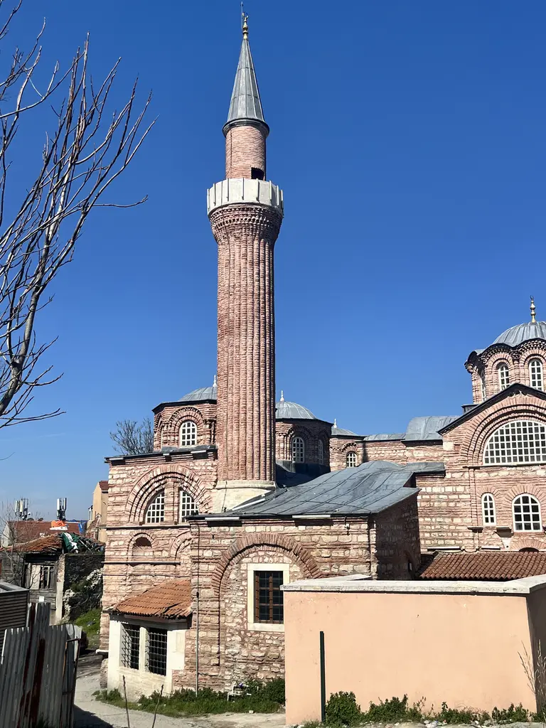 Vefa Kilise Camii'nin minaresi berrak kış göğüne karşı tam boy; yivli tuğla gövde, beyaz taş şerefe, mukarnaslı korniş, gri külah, sağda ana kubbe ve iki küçük kubbe.