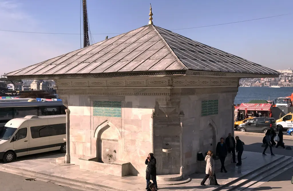 Üsküdar'da III. Ahmed Çeşmesi; kare planlı mermer gövde, geniş saçaklı çatı ve çevresinde dolaşan insanlar.