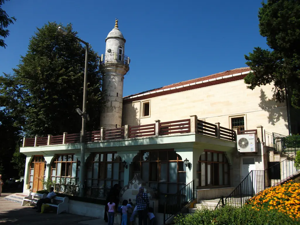 Anadolu Kavağı'nda Hz. Yuşa Camii; beyaz taş minare, kafesli pencereli tek katlı yapı, önde turuncu çiçekler ve ağaçlar.