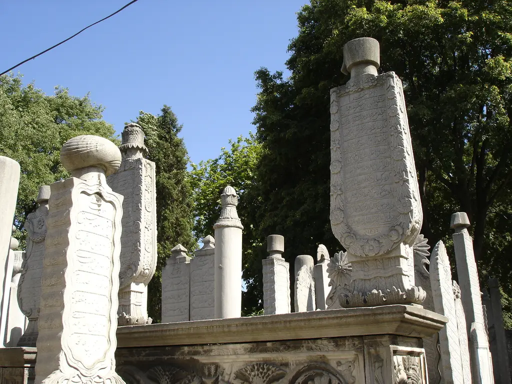 Eyüp Mezarlığı'nda kabir; taş lahit üzerinde başlıklı uzun mezar taşları, arkada ağaçlar ve açık mavi gökyüzü.
