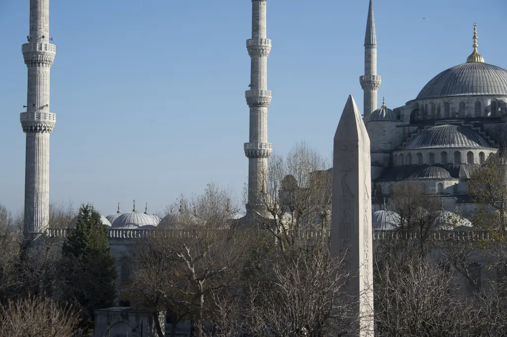 Dikilitaş ve Sultanahmet Camii; önde granit obelisk, arkada caminin kademeli kubbeleri ve ince minareleri, çıplak kış ağaçları.