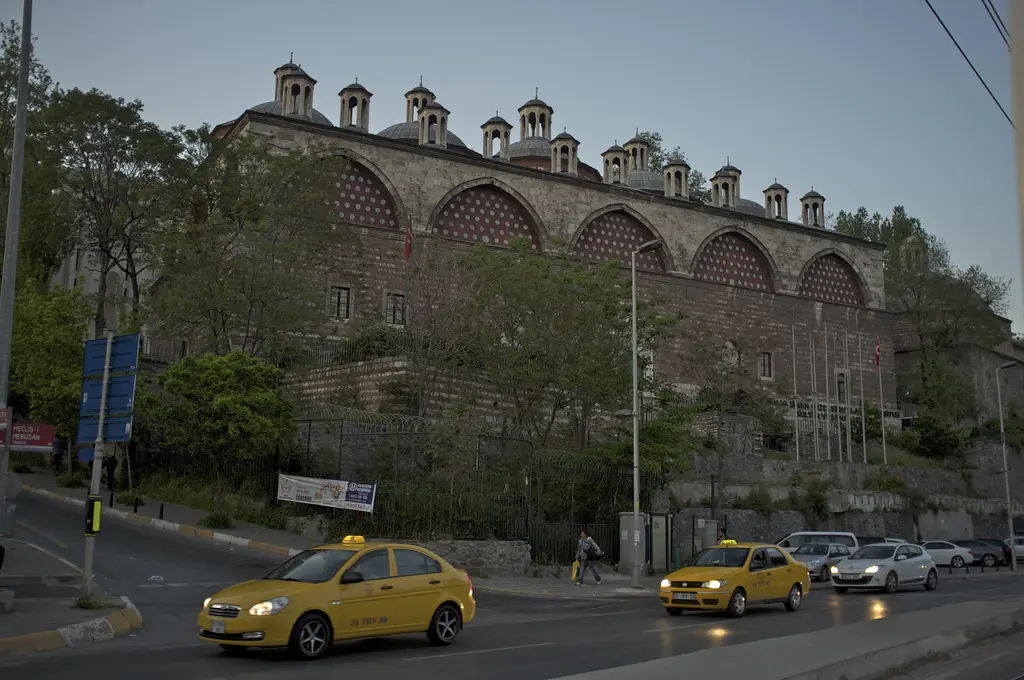 Meclis-i Mebusan Caddesi'nden Tophane-i Âmire; yolda sarı taksiler, arkada ağaçların üstünde yükselen kemerli taş bina.