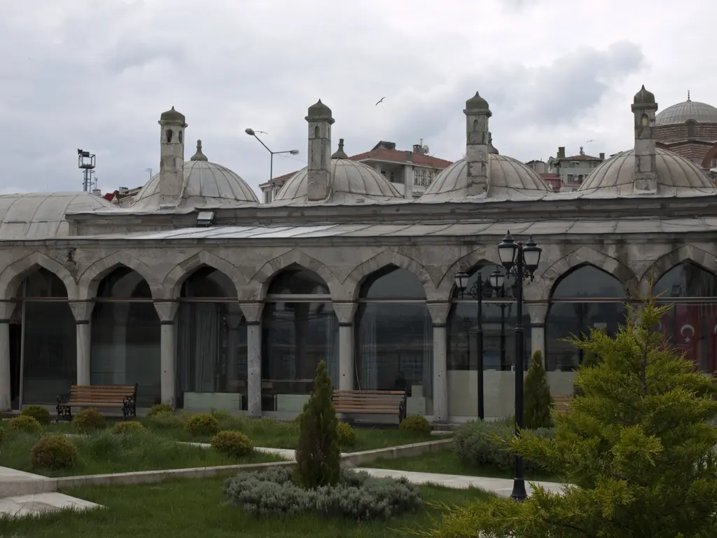 Şemsi Paşa Medresesi; sivri kemerli revak, kubbeli hücreler, bacalar, bahçedeki çalılar ve fenerler.