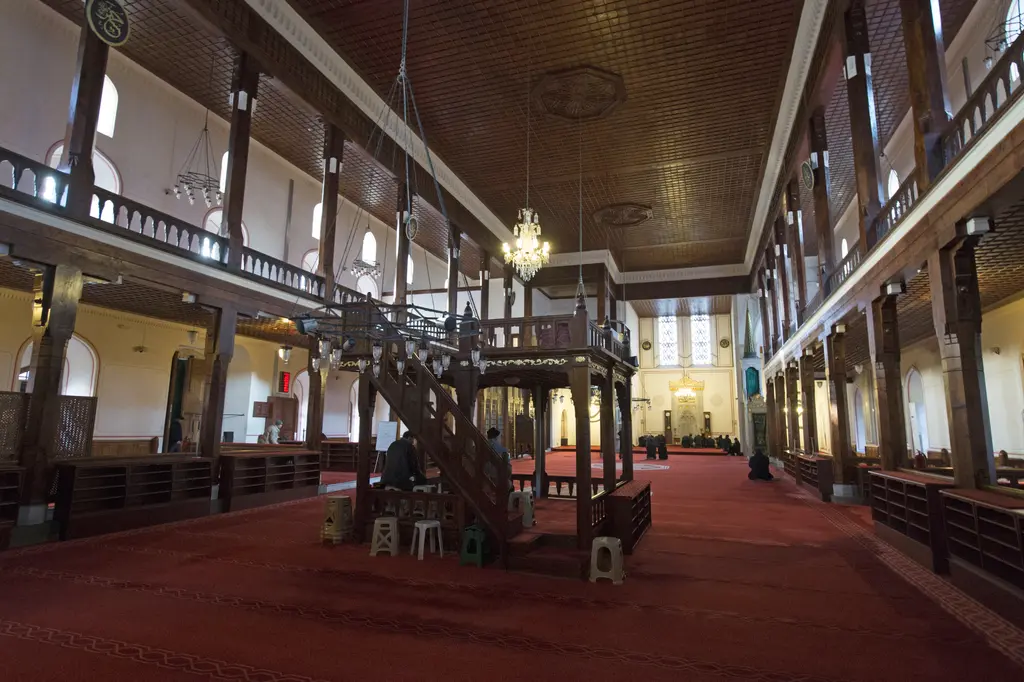 Arap Camii'nde minber; ahşap direkler arasında mermer minber, avize, kırmızı halı ve iki yanda mahfiller.