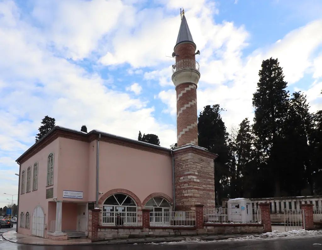 Karacaahmet'te Fethi Ahmed Paşa Camii; pembe sıvalı tek katlı cami, kemerli pencereler, tuğla minare ve arkada selviler.