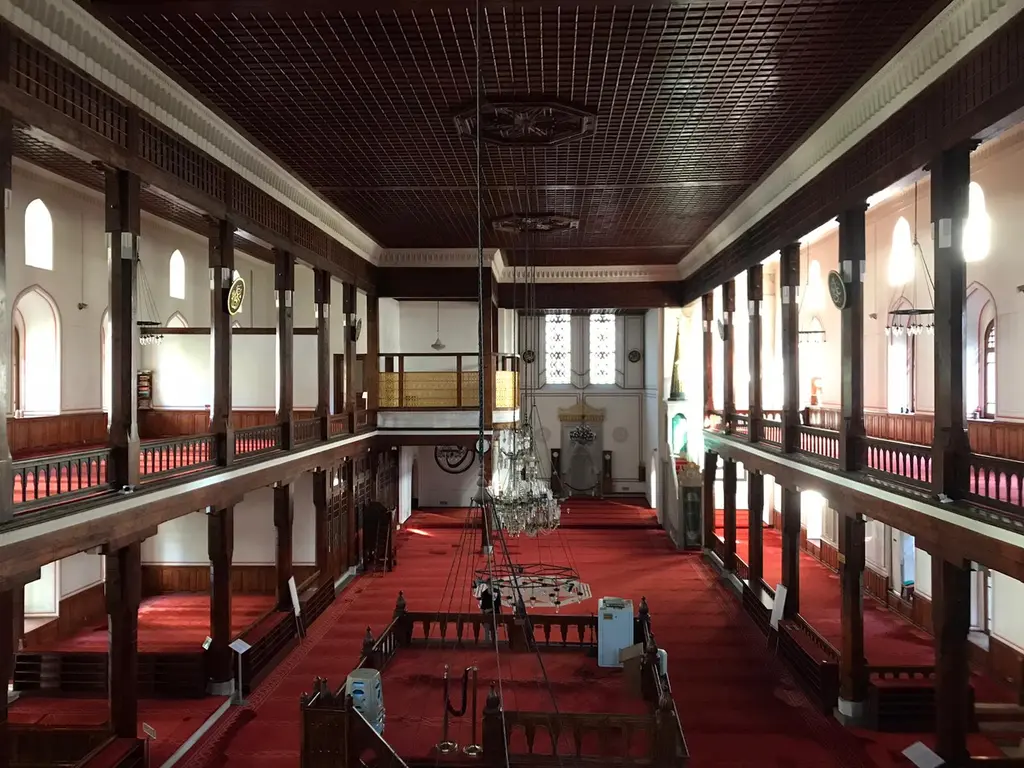 Arap Camii'nin içi; ahşap direklerle bölünmüş uzun harim, kırmızı halı, pencerelerden giren ışık ve ahşap tavan.