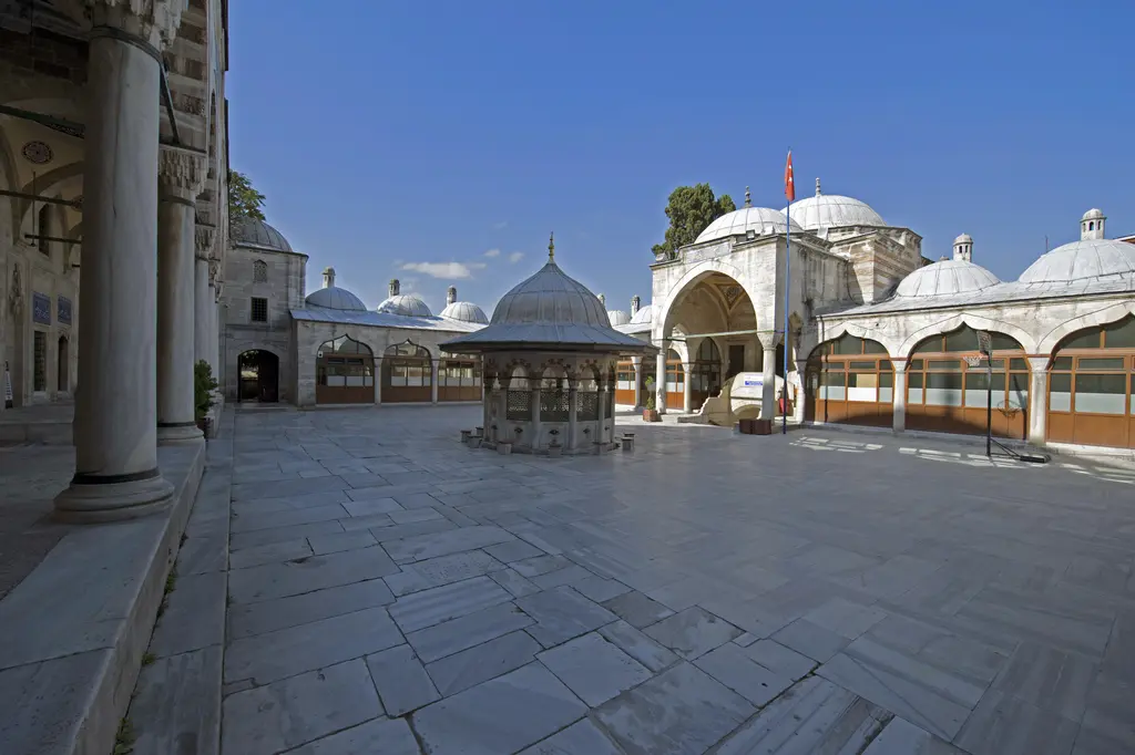 Sokullu Mehmed Paşa Camii'nde avlu ve medrese; sütunlu revak sırası, arkasındaki kubbeli hücreler, mermer döşeme ve bulutsuz mavi gökyüzü.