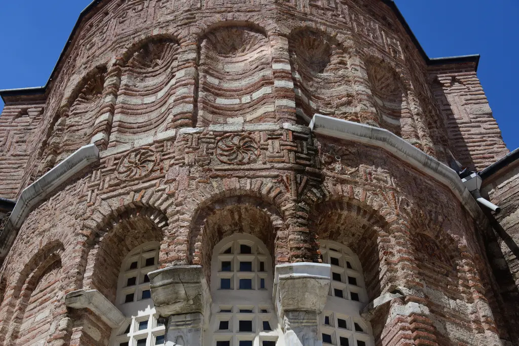 Fenari İsa Camii'nde apsisin üst zonu yakın planda; derin kör kemer nişleri, aralarında balıksırtı ve zikzak tuğla dolgular, beyaz mermer sütunçeler ve konsollar.